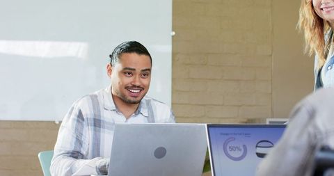 Diverse team collaborating around laptops in modern bright office with whiteboard