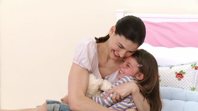 Happy scene capturing a mother hugging and playing with her daughter on a cozy bed. Ideal for use in family-oriented content, parenting blogs, advertising related to family lifestyle, and promotional material for family and children's products. Emphasizes love, warmth, and togetherness.