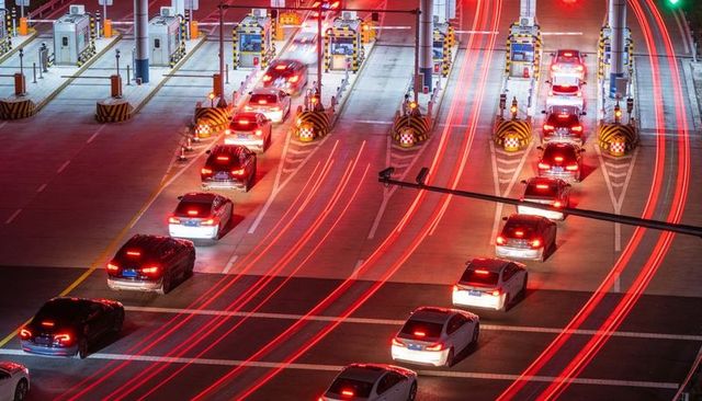 Curving red taillight trails at highway toll plaza at night, long exposure traffic motion