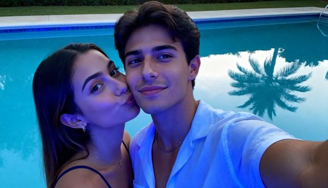 Young couple taking romantic selfie by blue backyard pool with palm reflection