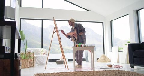 Indian man painting at easel in bright mountain-view home studio with natural light