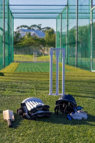 Cricket batting gear resting on turf inside practice net casting long shadows