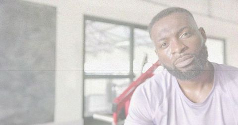 Black man sweating after workout standing in gym near red equipment and natural light