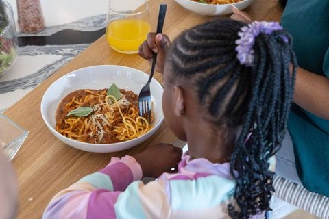 African american parent and child sharing spaghetti, child enjoying pasta with fork at home