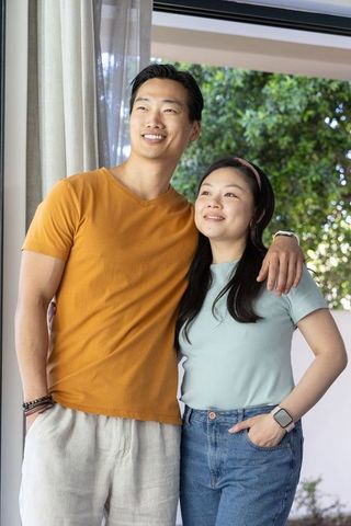 Asian couple standing at doorway looking out together on sunny porch showing warmth