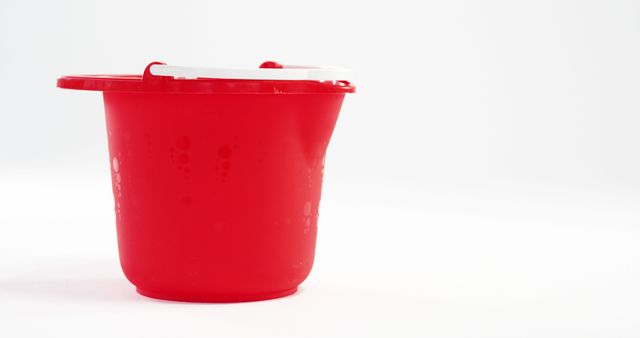 A red plastic bucket is featured against a white background, with copy space. Its simplicity and vibrant color make it stand out, suitable for various household and cleaning themes.