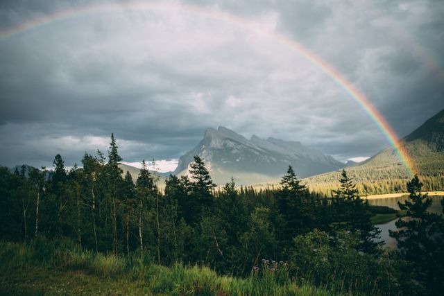 Shows a vibrant rainbow arcing across a sky filled with clouds above dense forest and towering mountains. Useful for promoting outdoor activities, nature conservation, travel destinations, and scenic wallpapers. Perfect for backgrounds, travel blogs, and environmental campaigns.