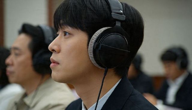 Asian man listening with studio headphones at conference, focusing attentively during meeting