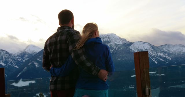 A Caucasian couple enjoys a breathtaking view of snow-capped mountains at sunset, with copy space. Their shared moment of admiration for the natural beauty underscores the romantic and serene atmosphere.