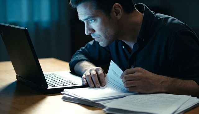 Focused man reading documents late night by laptop glow for remote work