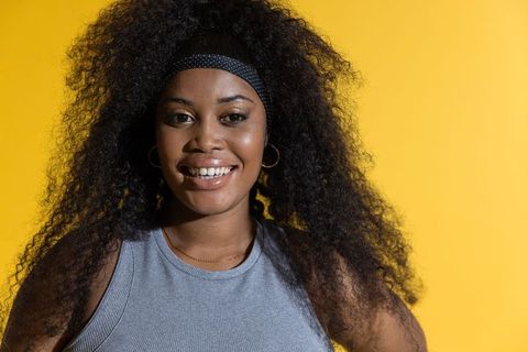 Smiling african american woman wearing black headband and gold hoops on yellow background
