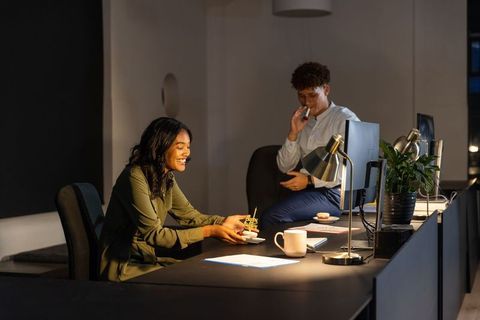 Coworkers celebrating late-night birthday in modern office with cake and warm desk lighting