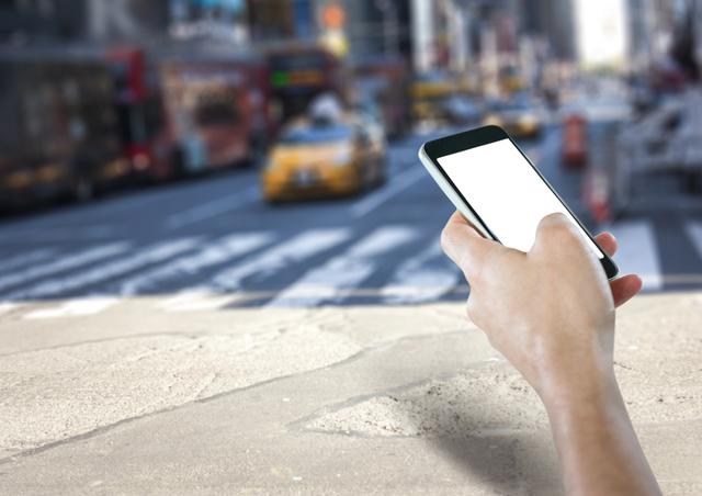Hand holding smartphone with blank screen in busy urban street with blurred taxis and pedestrians. Ideal for illustrating urban lifestyle, mobile technology, app usage, or navigation. Suitable for advertising, tech blogs, urban life content, or application demos.