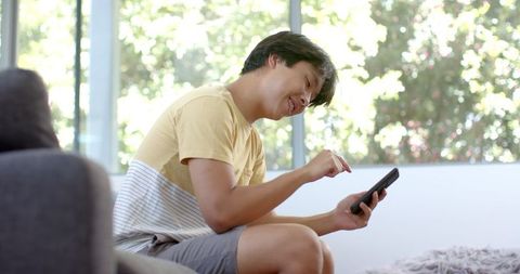 Young Asian Man Enjoying Smartphone Indoors