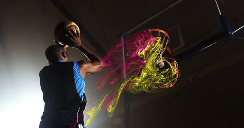 Basketball player dunking ball with neon motion trails at indoor court