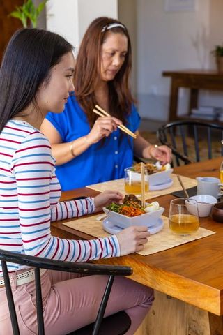Asian mother and daughter enjoying traditional noodle meal at home