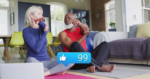 Active senior couple stretching together during bright home workout with laptop, yoga mats