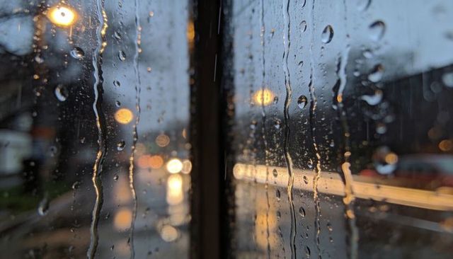 Rain-soaked window with vertical divider and warm streetlight bokeh at dusk, urban reflections