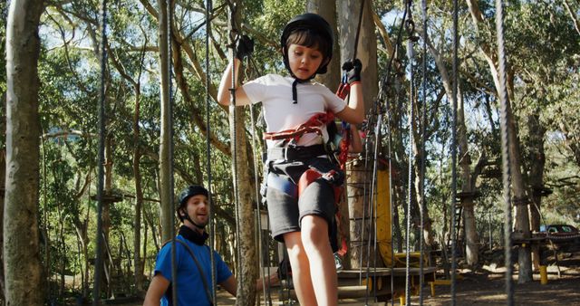 A young child is engaged in an outdoor adventure activity, wearing safety gear and being watched over by an adult male, with copy space. The setting suggests a bonding experience, a father-son moment, emphasizing trust and encouragement in a recreational environment.