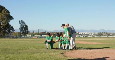 Baseball team kneeling while coach giving pep talk on grass infield showcasing leadership