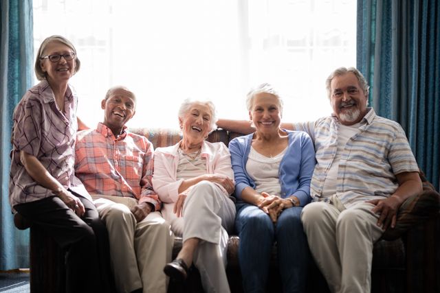 Group of senior friends sitting on a couch, smiling and enjoying each other's company in a nursing home. Ideal for use in advertisements for senior living communities, retirement homes, healthcare services, and companionship programs. Perfect for illustrating themes of friendship, happiness, and quality of life for the elderly.