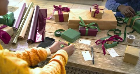 Couple wrapping holiday gifts with ribbons and brown paper on sunlit craft table