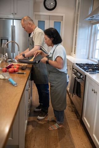Asian couple cooking in modern kitchen, senior woman flipping pan at island preparing meal