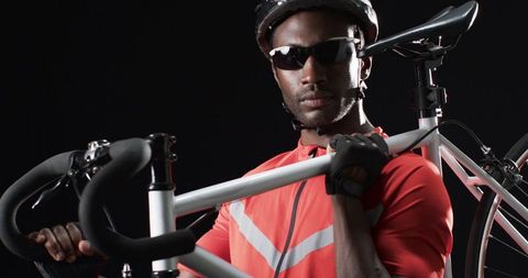 Confident cyclist holding bicycle against black background