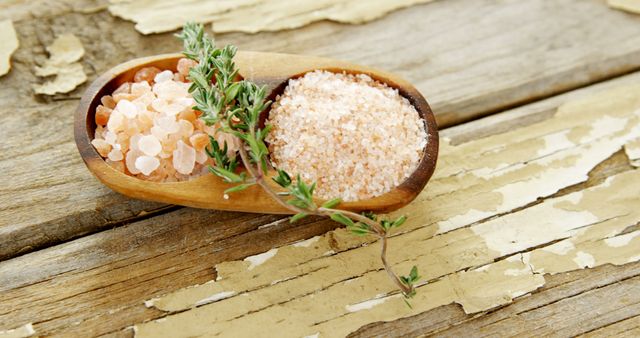 Himalayan pink salt and fresh thyme are presented in a wooden spoon on a rustic table, with copy space. These ingredients are often used in cooking to enhance flavor and add a gourmet touch to dishes.