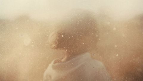 Backlit woman standing in warm vintage haze with floating dust particles