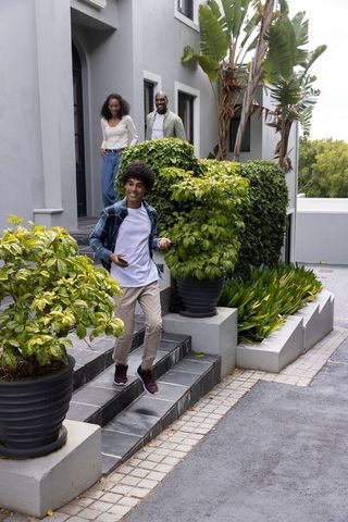 Teenager descending steps while parents watching at doorway holding smartphone near planters