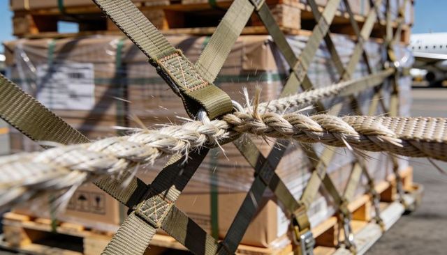 Close-up braided rope and olive-green webbing securing palletized freight on airport ramp
