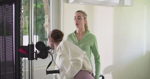 Female personal trainer coaching client on cable machine for strength training in studio