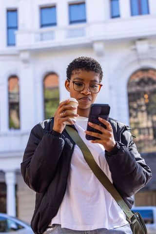 Urban commuter checking phone while holding coffee outside historic city building