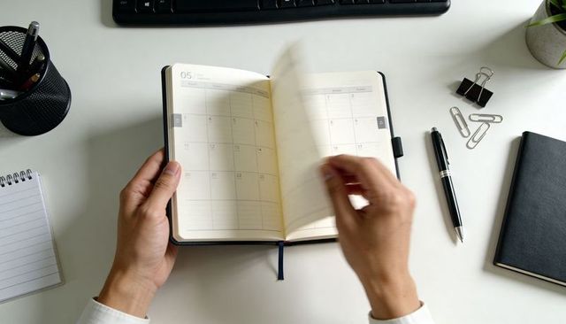 Hands flipping through monthly planner on white desk for productivity and time management