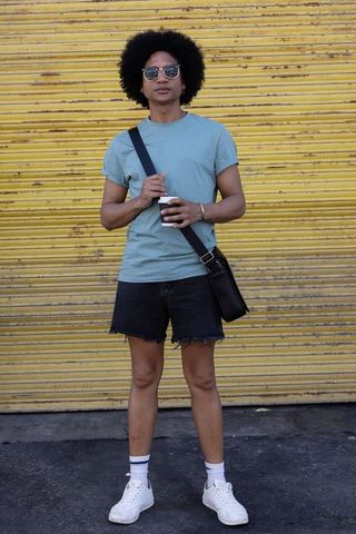 African american man standing with coffee and crossbody bag against yellow metal shutter