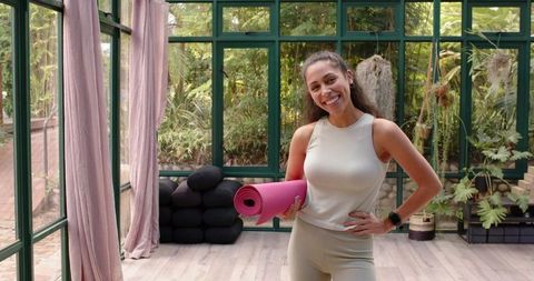 Woman Holding Pink Yoga Mat in Bright and Airy Yoga Studio