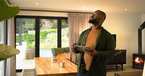 African American man using tablet surveying modern cozy dining room and open plan living area