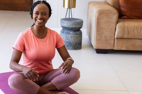 African american woman smiling on yoga mat wearing smartwatch during home wellness routine