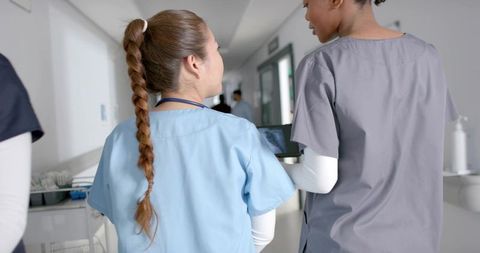 Nurses walking hospital corridor checking tablet and stethoscope collaborating on care