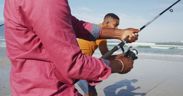 Two African American men enjoying fishing on a sunny beach. Perfect for themes of leisure activity, outdoor hobbies, bonding, or promoting travel and nature experiences.