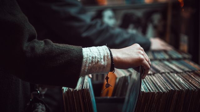 This image shows a person browsing through vinyl records in a store, suggesting a nostalgic appreciation for retro music formats. With a close-up view of the hand and record sleeves, it captures the essence of a detailed collection search. This can be used in websites, magazines, or advertisements related to music, vintage collections, retail, and hobbies.
