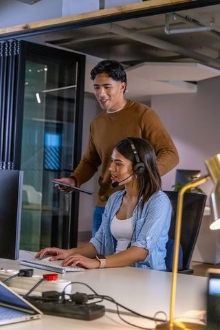 Young colleagues collaborating at open office workstation with headset and tablet