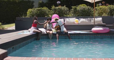 African american friends relaxing by backyard pool playing guitar and enjoying sunny summer afternoo