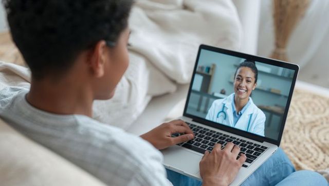 Teenager consulting doctor via laptop, smiling clinician on screen, telemedicine visit