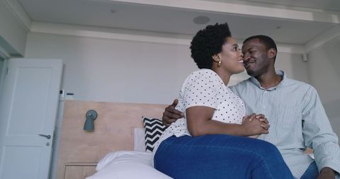 African American couple sitting on bed cuddling and holding hands in modern minimalist bedroom
