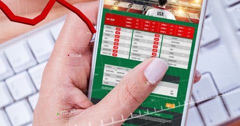 Thumb tapping smartphone sports betting app showing live odds and analytics dashboard