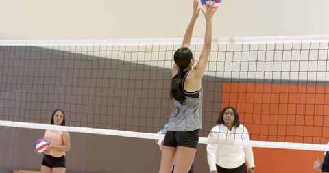 Volleyball practice female player jumping to block ball under african american coach