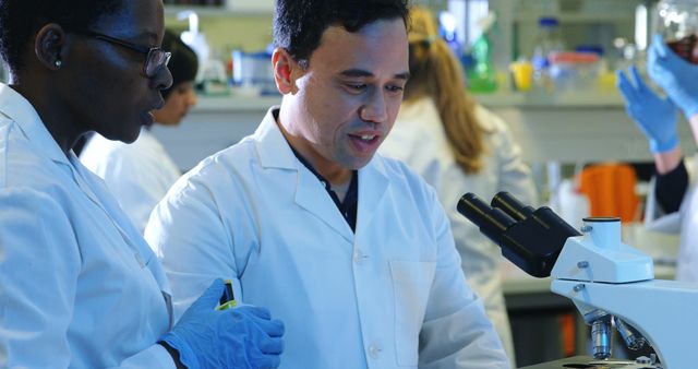 Scientists working together in a research laboratory. One scientist looking at a phone, while the other is standing next to a microscope. This image can be used to highlight scientific collaboration, teamwork, and laboratory research processes. Suitable for educational materials, scientific journals, and promotional content related to laboratory work, science, and technology.