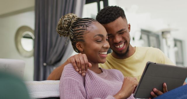 Happy african american couple sitting on sofa and relaxing with tablet. Lifestyle, relationship, spending free time together concept.